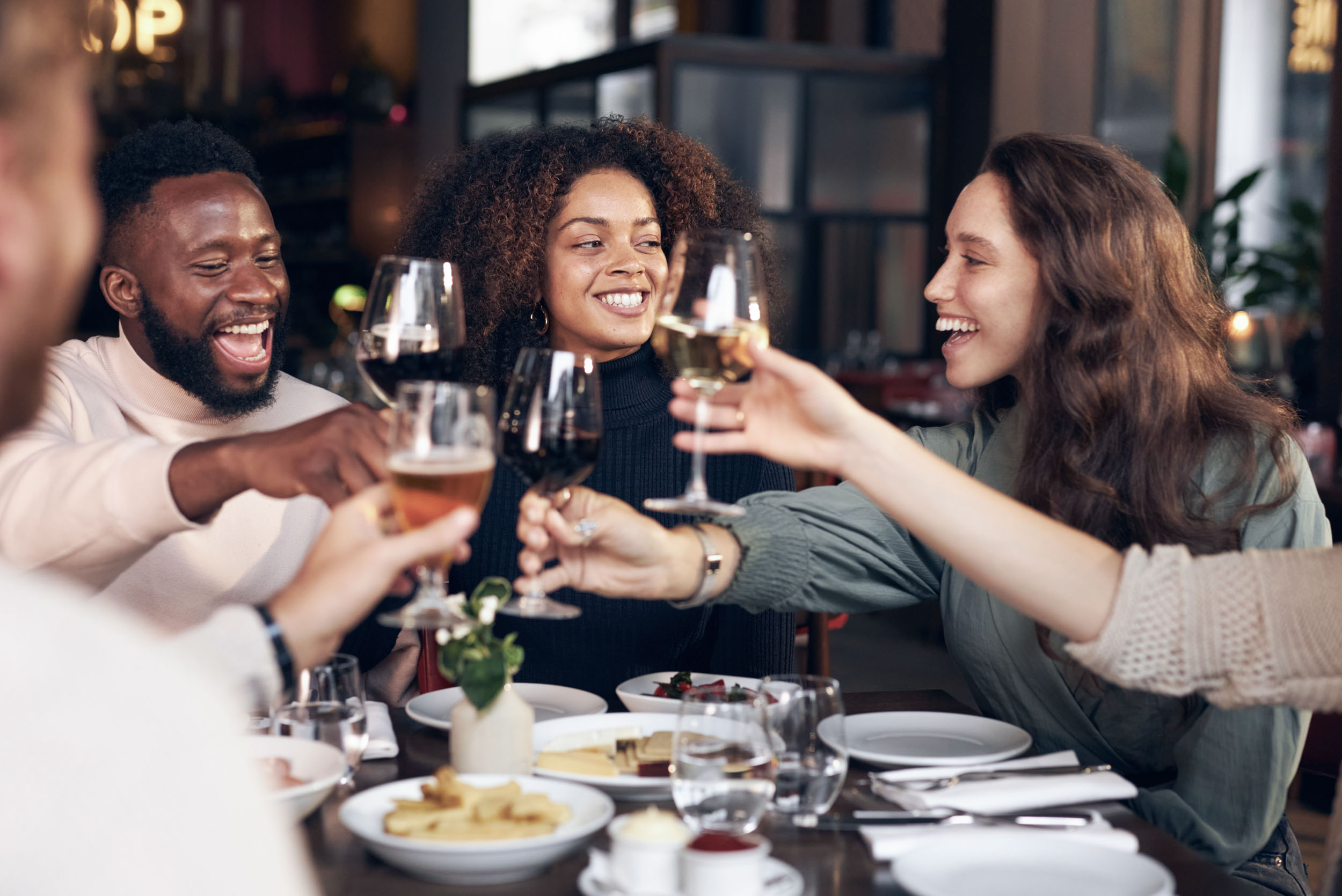A group of happy diverse friends raising wine and beer glasses in a toast at a restaurant table