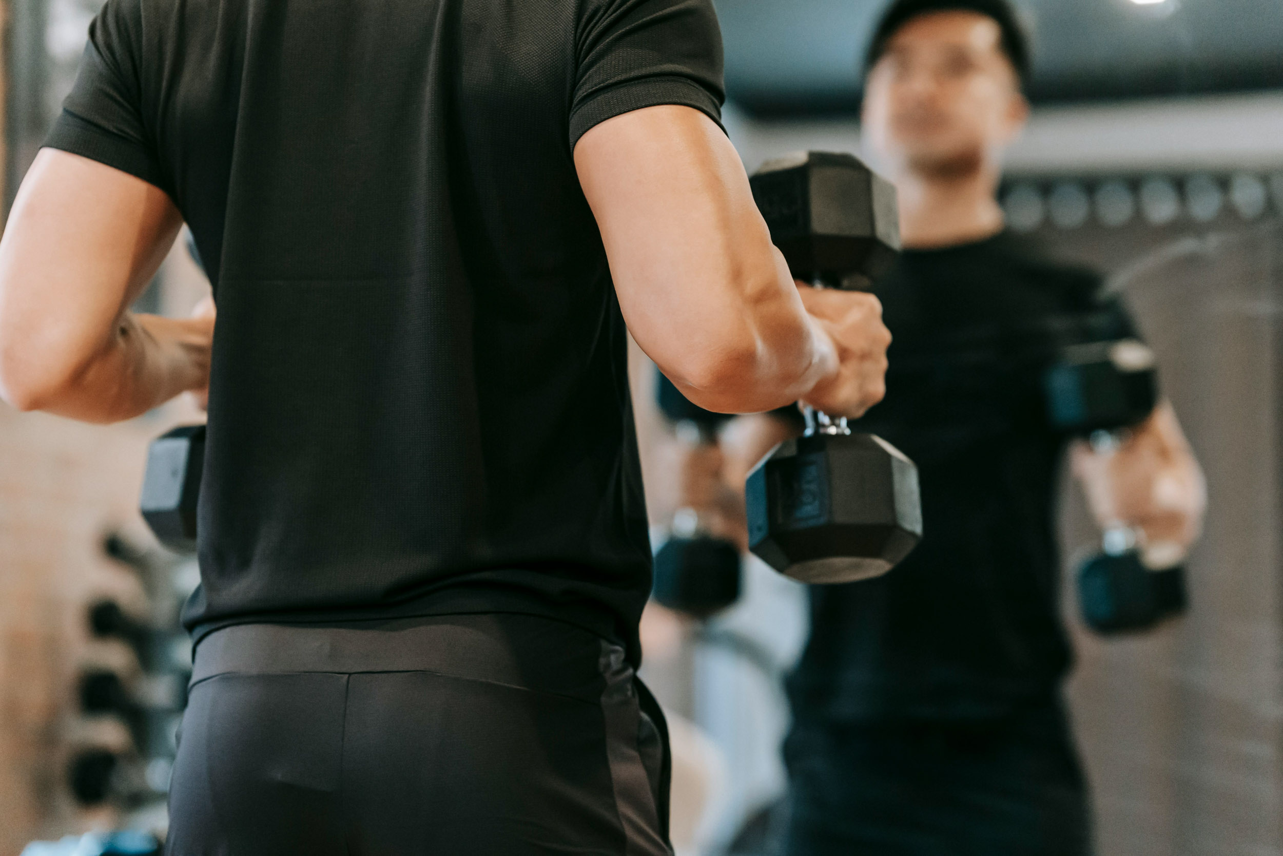 A man lifting hexagonal dumbbells while looking at his reflection in a gym mirror